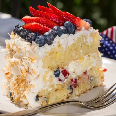 Patriotic cream cheese frosting swirls topping the moist Pineapple Coconut God Bless America Cake slice.
