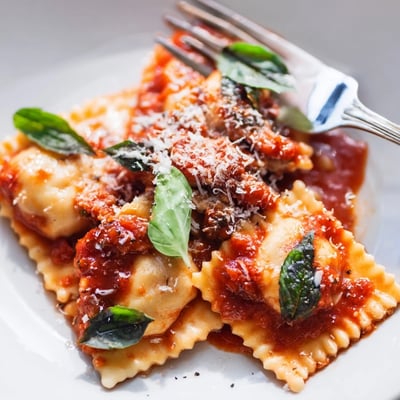 Golden-brown ravioli with chicken and mushrooms sit in a pool of vibrant red tomato sauce.
