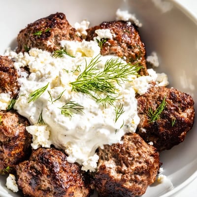 Golden Greek meatball bowl topped with crumbled feta and crisp cherry tomatoes